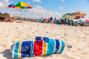 Image of beach towel and sunglasses laying on the sand at a busy beach