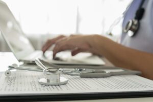 Image of healthcare worker typing on laptop with stethoscope