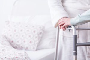 Image of elderly woman with walker standing beside her bed