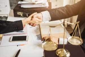 Image of two people shaking hands over a desk covered in paperwork next to a legal scale