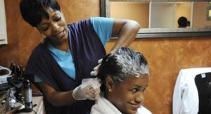 Image of woman applying hair relaxer to client in salon