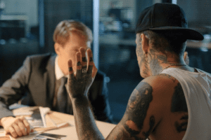 Image of man with tattoos talking to man in suit