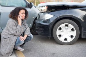 Image of a lady squatting down next to car crash making a phone call