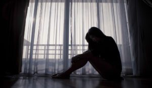 Image of sad woman sitting in a dark room in front of a window