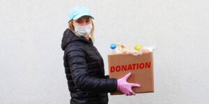 Image of a woman in a mask with gloves carrying a donations box