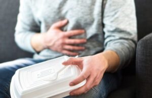 Image of person holding a takeout food container with their hand on their stomach in pain