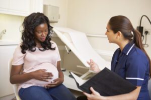 Image of pregnant woman sitting on an exam table while talking to a medical professional