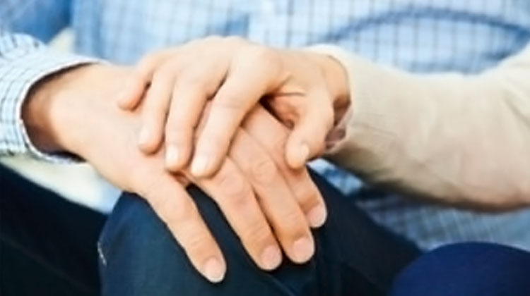 Up close image of two people holding hands in a comforting way