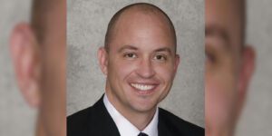 Image of man with black suite, white button up shirt, and black tie