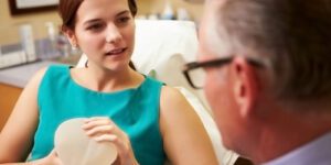 Image of woman holding a breast implant and talking to a doctor