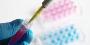 Up close image of a gloved hand filling a test tube with pink liquid