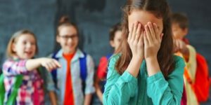 Image of young children bullying a girl who has her hands covering her face