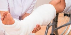 Image of a medical professional checking on a person with a leg cast in a wheel chair