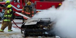 Image of vehicle fire with firefighters spraying the vehicle with a hose