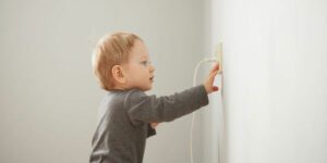 Image of a young toddler touching an electrical outlet with cord plugged in