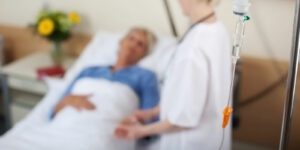 Image of medical professional checking on a patient in bed with an IV drip in the foreground