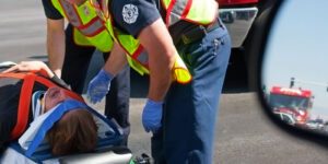 Image of person in pain on a stretcher with head restraint being cared for by paramedics