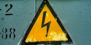 Image of a yellow and black triangle sign with a lightning bolt with an arrow on the end on a green wall