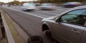 Image of car with missing tire on shoulder of a busy highway