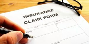 Image of hand filling out insurance claim form with a pen and sunglasses nearby