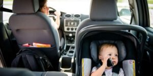 Image of woman driving with baby in a rear facing car seat pretending to talk on the phone