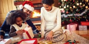 Image of happy family opening gifts by a Christmas tree and fireplace