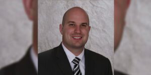 Image of a man in a black suite with a black and white tie and white button up shirt