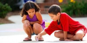 Image of two children drawing outside with sidewalk chalk