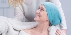 Image of a cancer patient in a head wrap being covered with a cozy blanket by someone