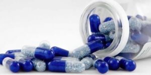 Image of blue capsule pills spilling from a clear bottle