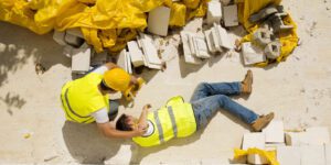 Image of injured construction worker in safety gear on a worksite being assisted by coworker