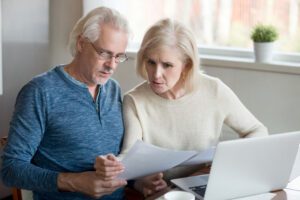 Senior couple reading paperwork in front of laptop