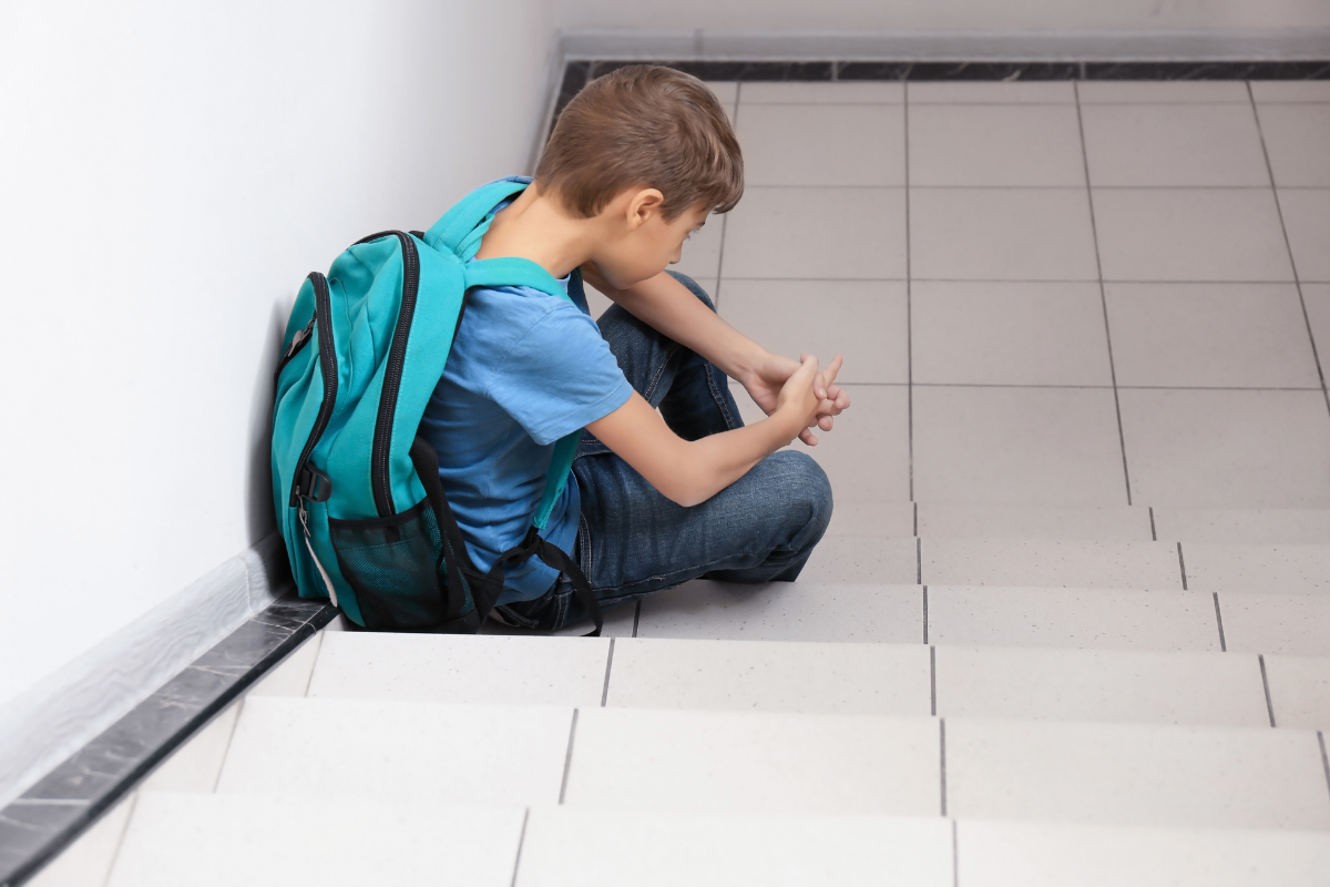 Sad adolescent boy sitting at the bottom of stairs with a backpack