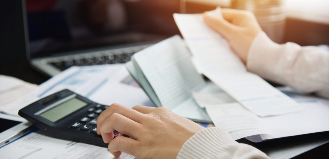 Image of a woman calculating bills with a calculator and laptop