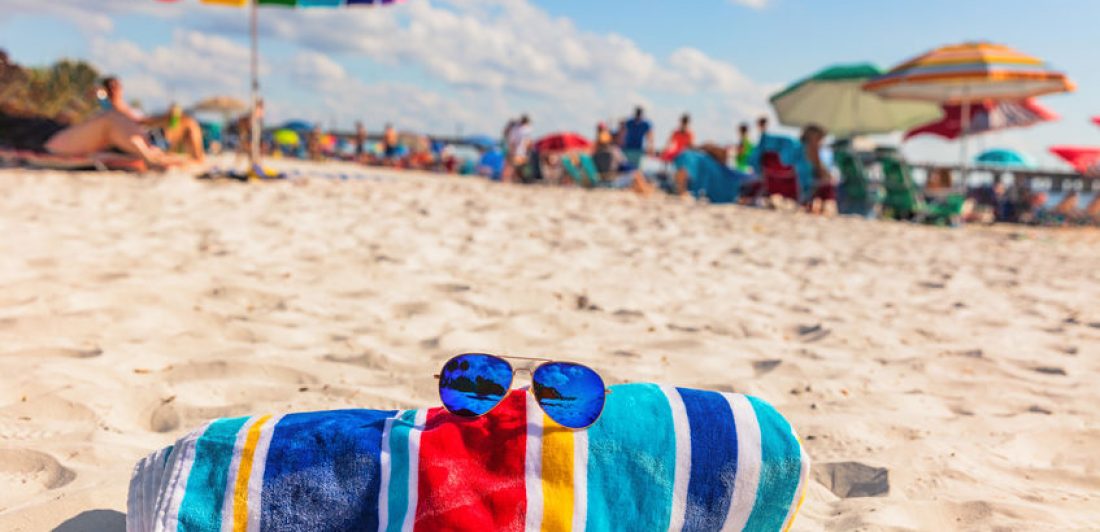 Image of beach towel and sunglasses laying on the sand at a busy beach