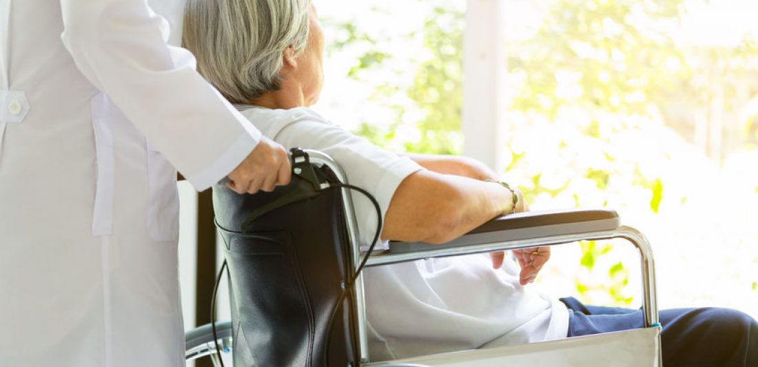 Image of medical professional pushing elderly woman in wheelchair