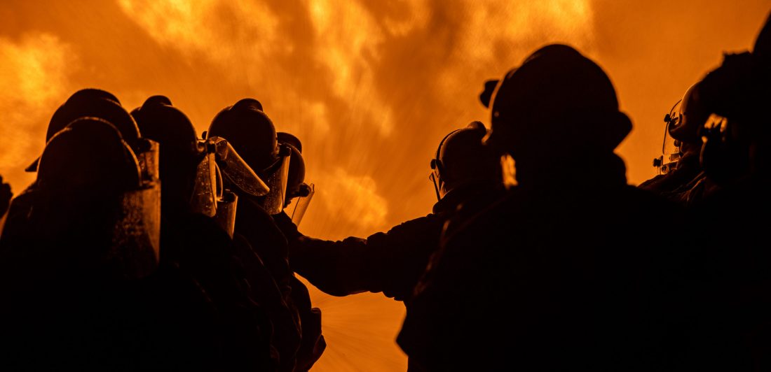 Image of firefighters standing in front of a large fire