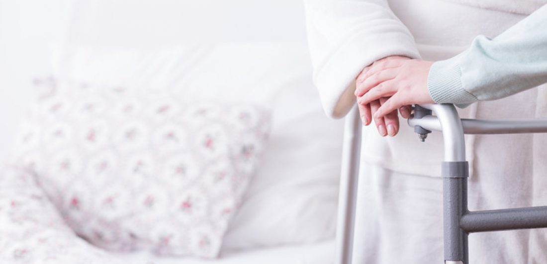 Image of elderly woman with walker standing beside her bed