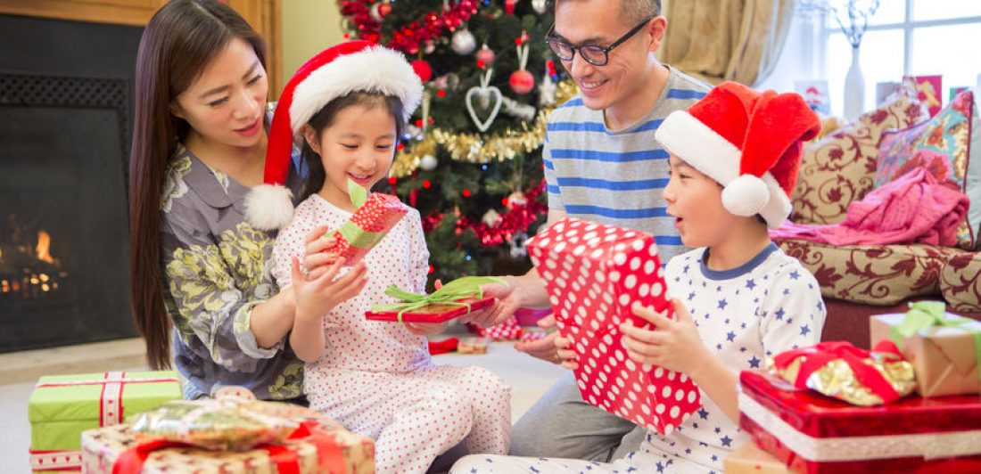 Image of happy family openings gifts by christmas tree and fireplace