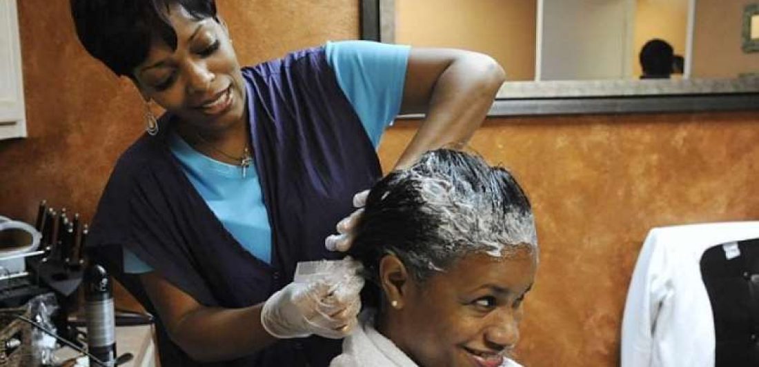 Image of woman applying hair relaxer to client in salon