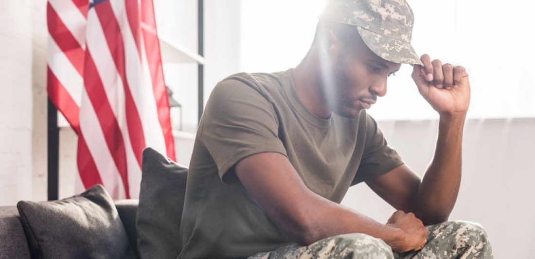 Image of sad man sitting in military uniform with flag in the background