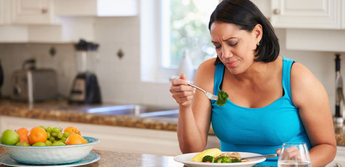 Image of woman looking unhappy while eating a plate of food