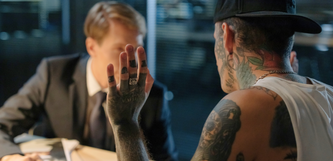 Image of man with tattoos talking to man in suit