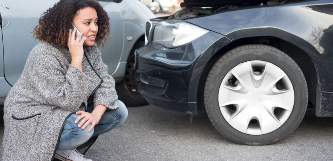 Image of a lady squatting down next to car crash making a phone call