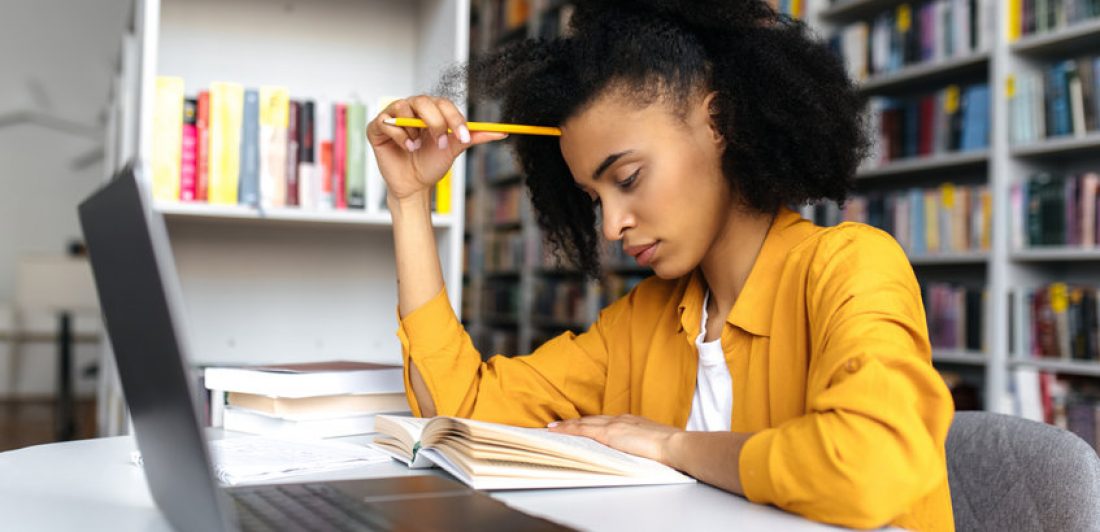 Image of girl sitting at a laptop reading a book