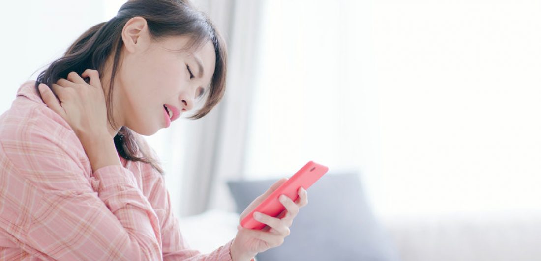 Image of woman holding her neck in pain while looking at her cell phone