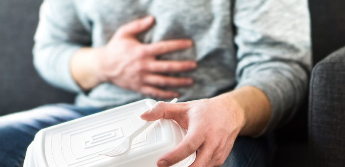 Image of person holding a takeout food container with their hand on their stomach in pain