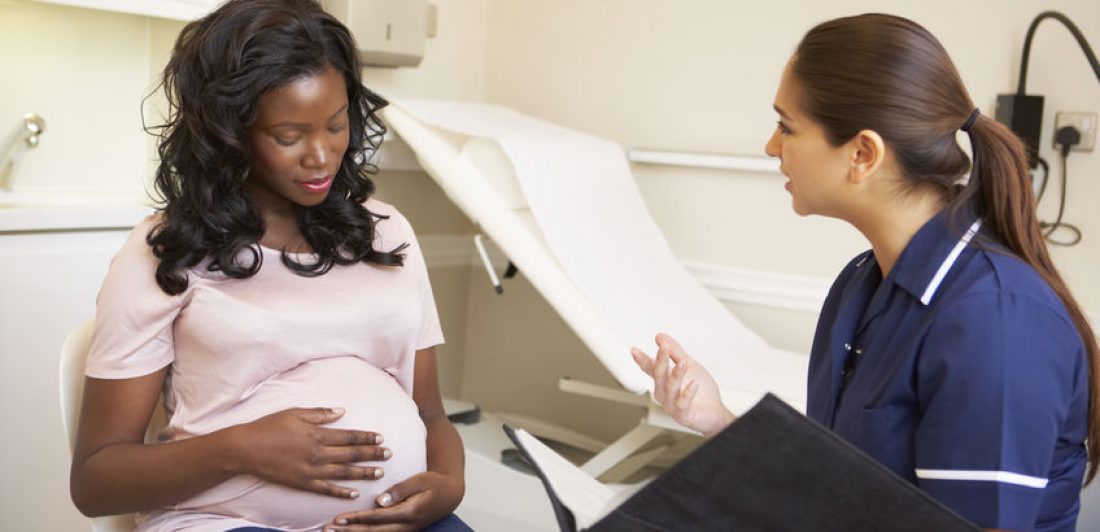 Image of pregnant woman sitting on an exam table while talking to a medical professional