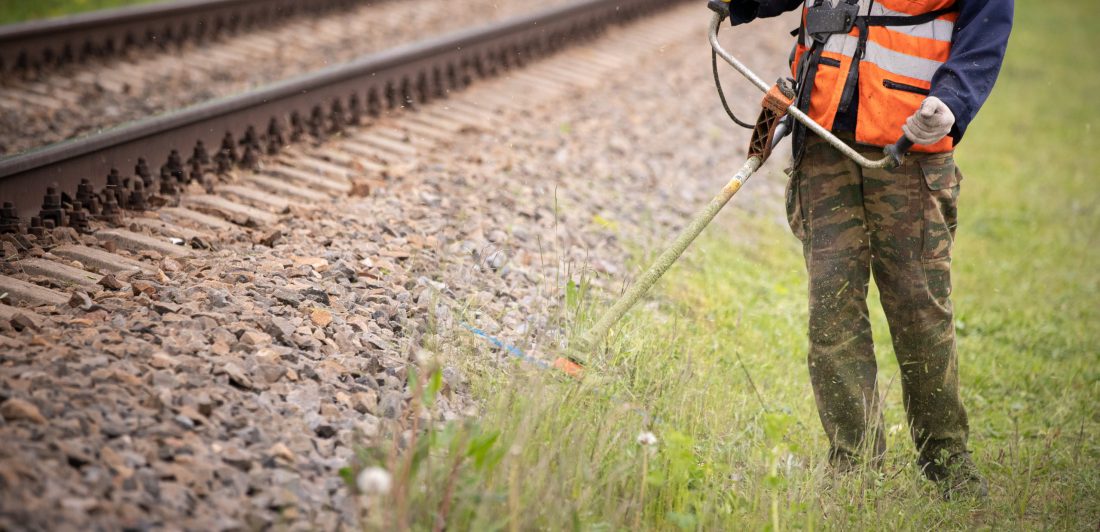 Image or worker cutting grass near train track