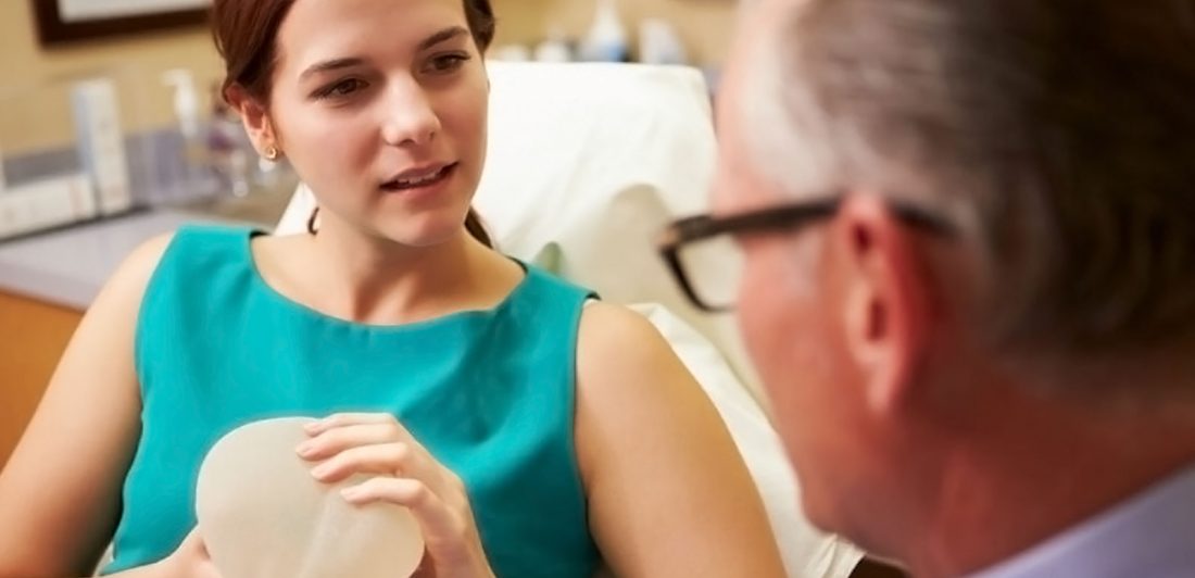 Image of woman holding a breast implant and talking to a doctor